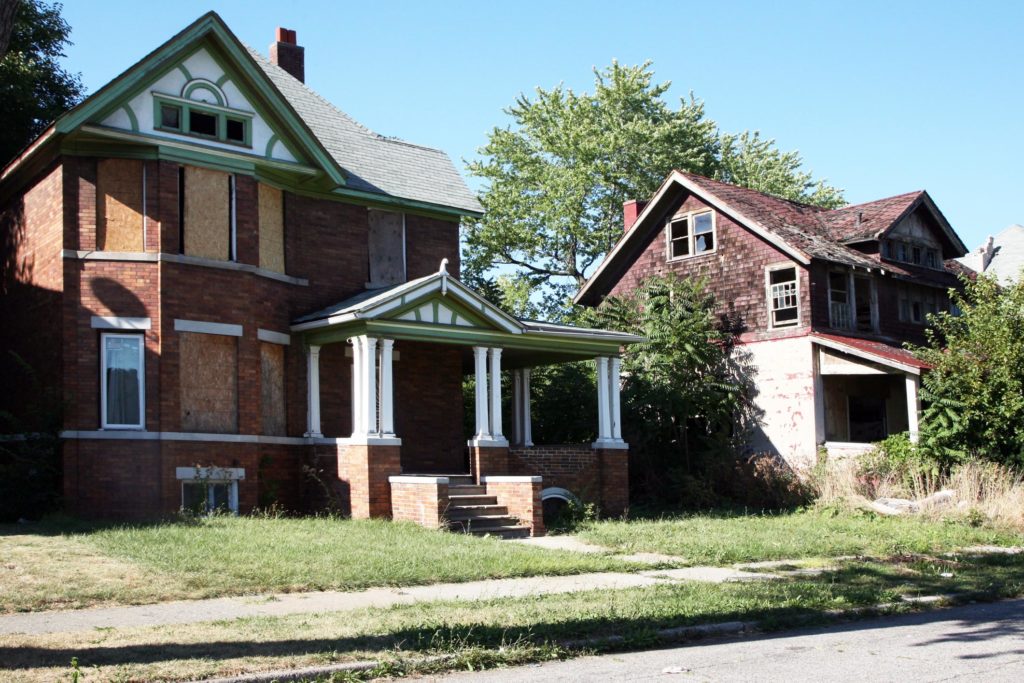 real estate iBuyer distressed house, with weeds and boarded up windows